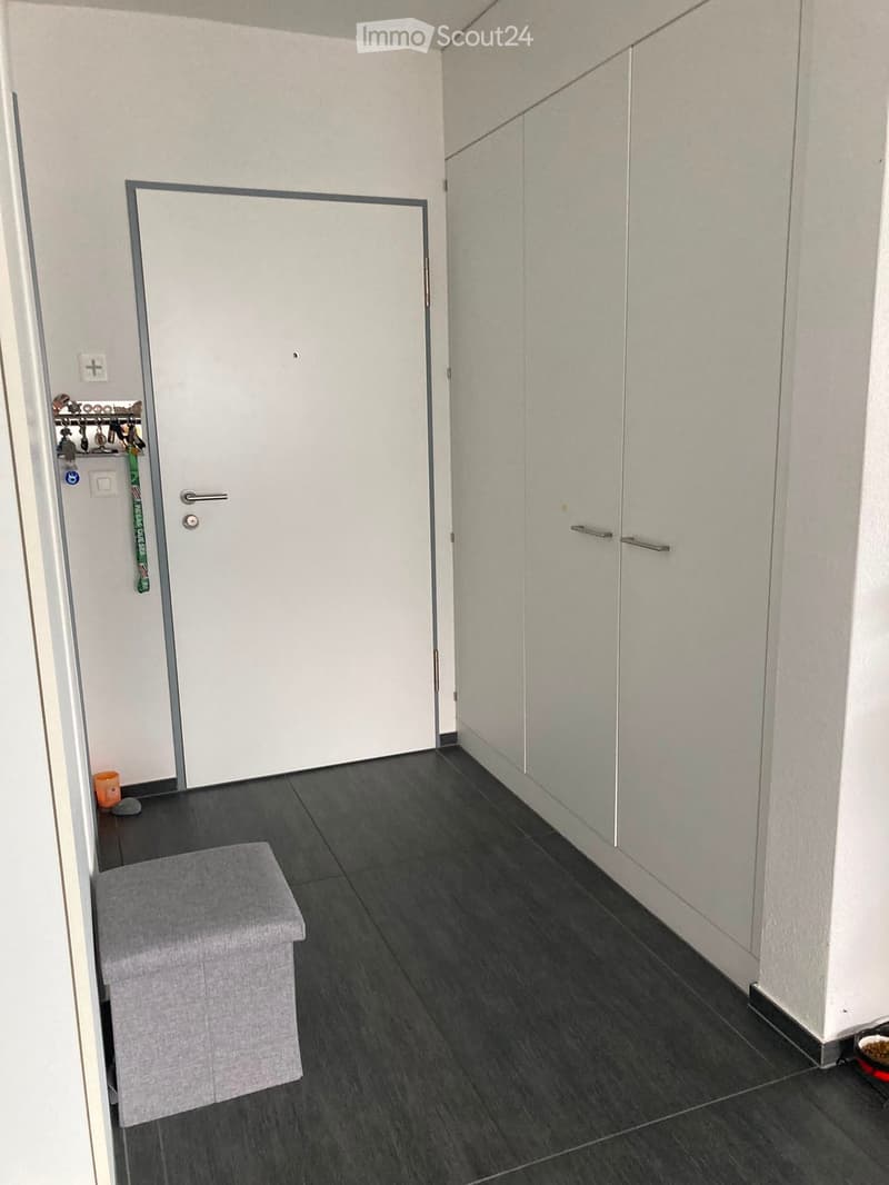 Hallway with dark tiled floor, white walls, grey stool, and a small orange cup on the floor.