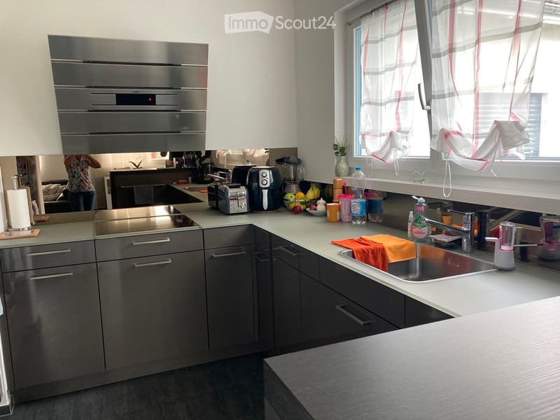 Modern kitchen with stainless steel appliances, grey cabinets, and a white countertop. Features an oven, toaster, blender, and a sink with a faucet.