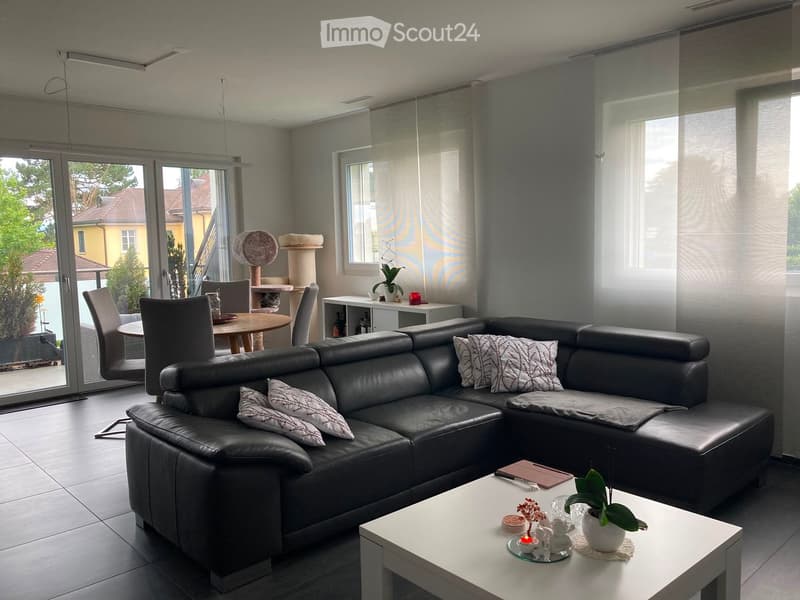 Modern living room with a black leather sofa, coffee table, dining area with chairs and table, cat tree, and decorative items.