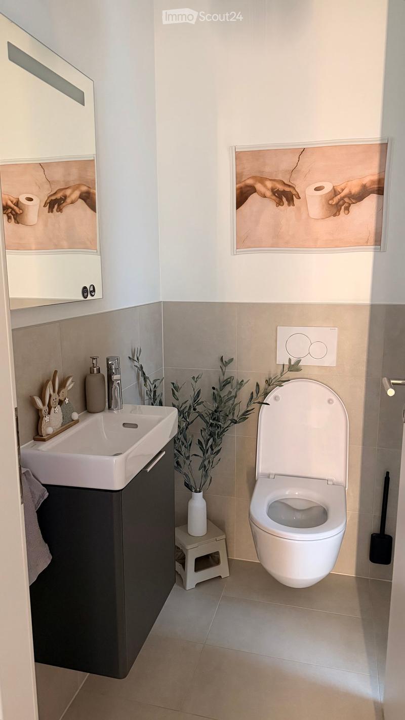 Modern bathroom with a white sink, chrome faucet, toilet, mirror, decorative rabbit figurines, and a small plant in a vase on a stool.