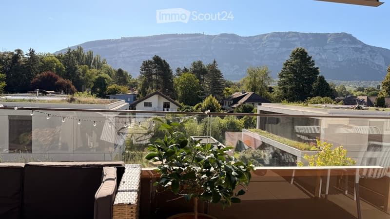 Balcony with a view of mountains, featuring a sofa, table, chair, and potted plant.