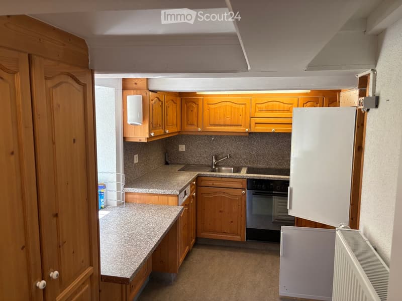 Compact kitchen with wooden cabinets, granite countertop, sink, faucet, oven, refrigerator, and radiator.