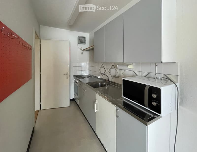 Modern kitchen with white cabinets, stainless steel sink, microwave, and oven. Features a red accent wall and a door leading to another room.