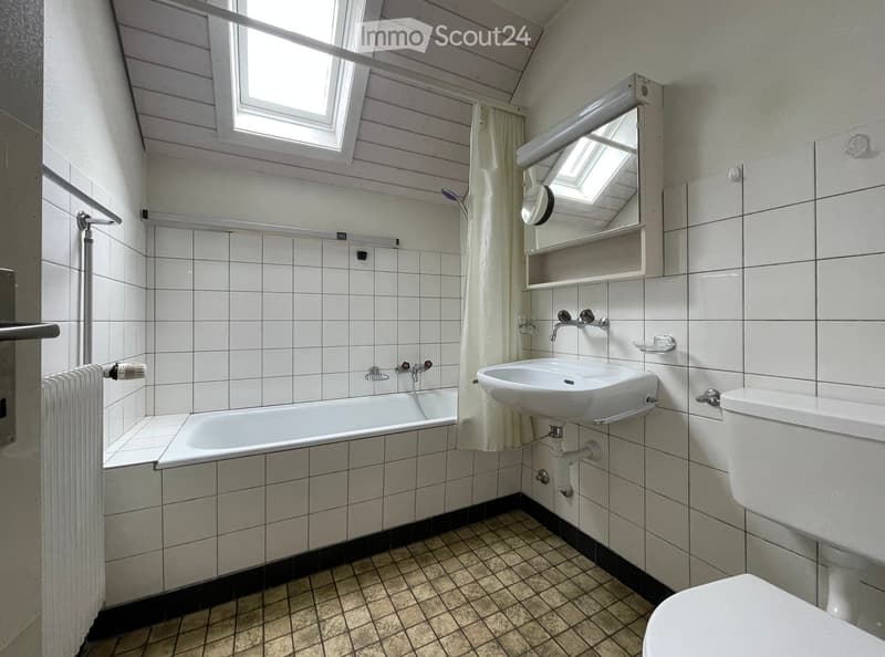Bathroom with white tiled walls, a bathtub, a sink, a toilet, a mirror, and a window with a curtain.