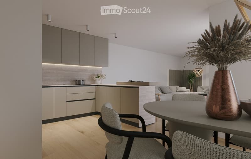 Modern open-plan living and dining area with a grey sofa, round dining table, chairs, and a tall vase with dried plants. The kitchen features sleek cabinets, a central island, and built-in lighting.