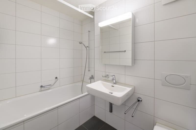 Modern bathroom with white tiled walls, a bathtub, a sink with a mirror, and a showerhead.