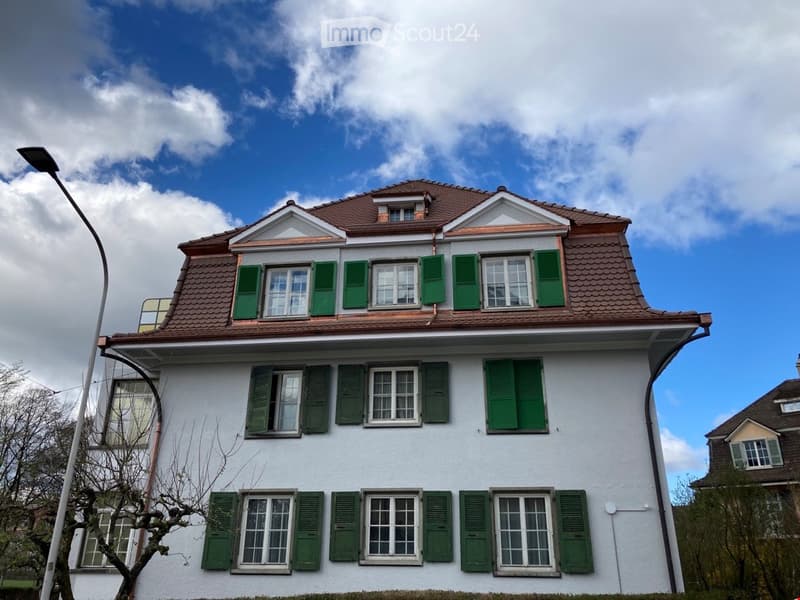 Two-story house with white exterior, green shutters, and a brown tiled roof.