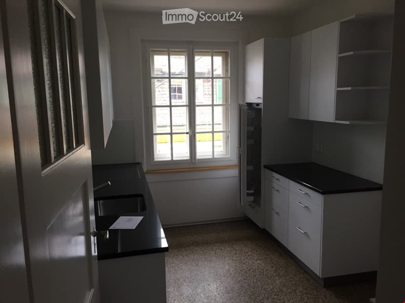 Modern kitchen with white cabinets, black countertops, and a stainless steel sink. The space is clean and well-lit with natural light from a window.