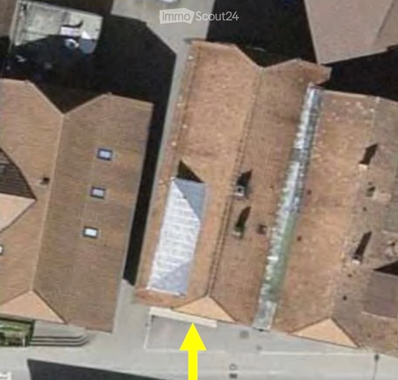 Aerial view of a multi-story building with a flat roof and multiple windows, surrounded by other structures.