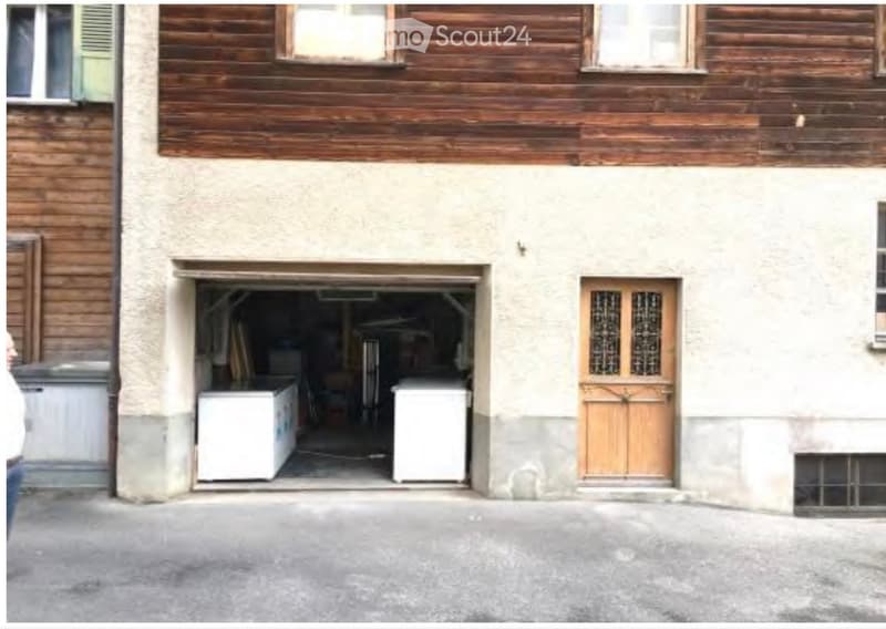 Facade of a two-story building with a garage entrance, wooden doors, and visible appliances inside the garage.