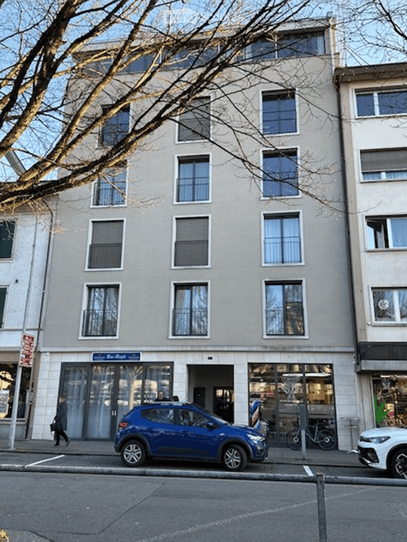 A multi-story building with large windows and a storefront at the ground level, with a blue car parked in front.
