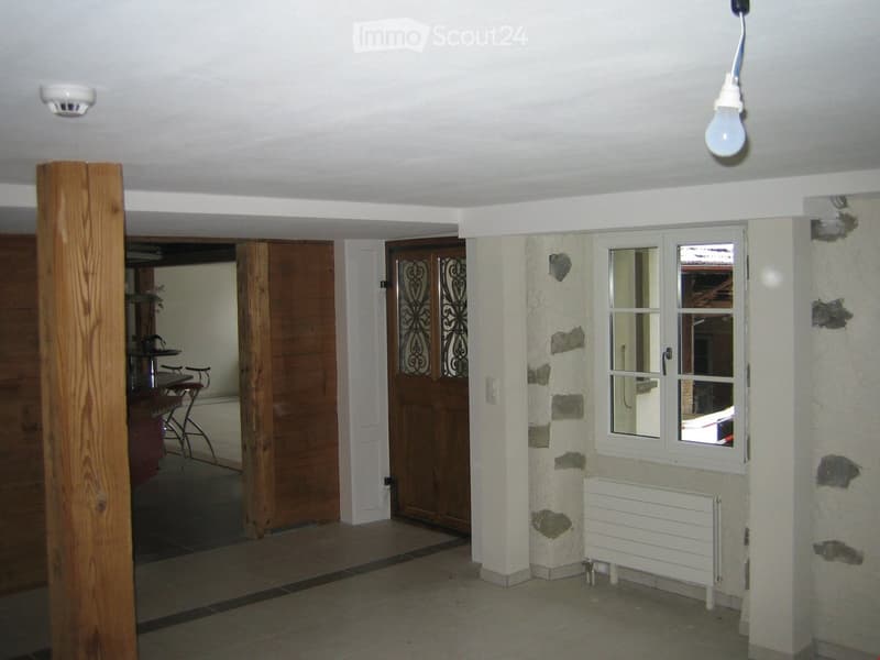 Empty room with tiled floor, white walls, wooden pillar, and a window with a view of the outside. No furniture or equipment is present.