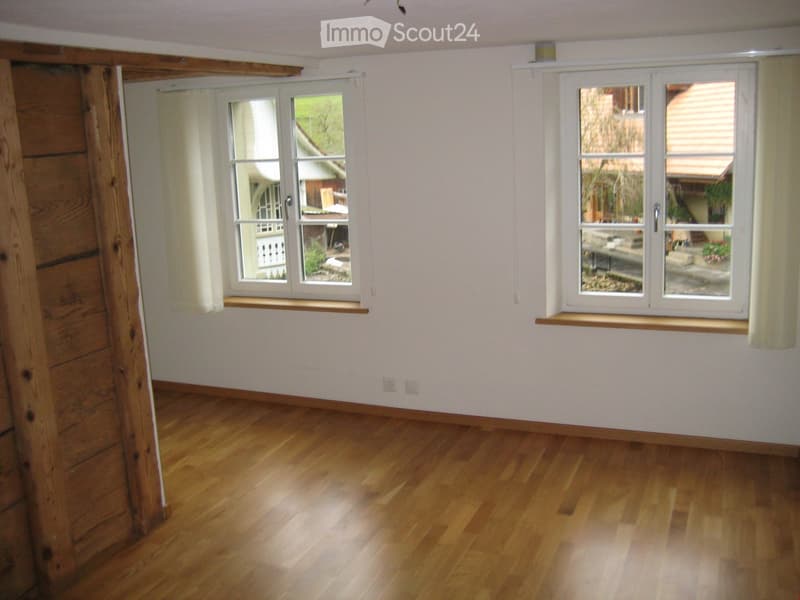 Empty room with wooden flooring, white walls, and large windows with wooden sills. The room is unfurnished and has natural light from the windows.