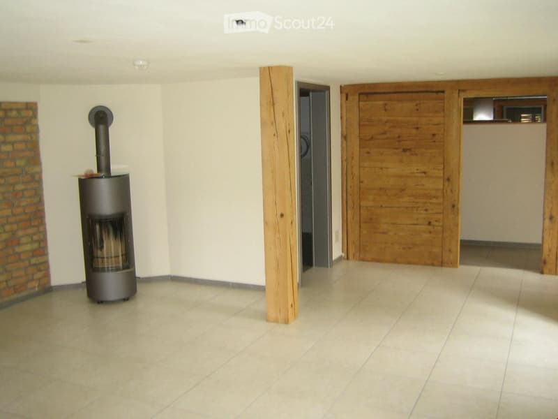 Empty room with tiled floor, white walls, a central wooden pillar, and a modern metal fireplace with a chimney on the left side.