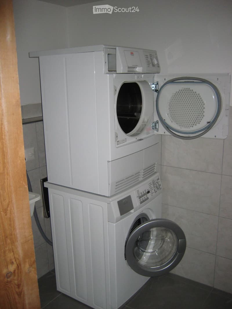 A compact bathroom with a stacked washing machine and dryer unit, both white, with open doors showing the interior.