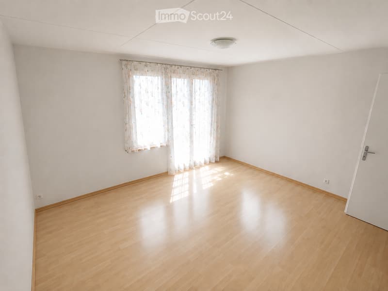 Empty room with light wooden flooring, white walls, and a window with sheer curtains. No furniture or equipment is present.
