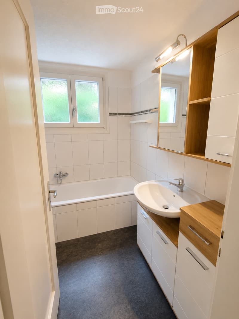 Modern bathroom with white tiles, a bathtub, a sink with wooden countertop, and a mirrored cabinet.
