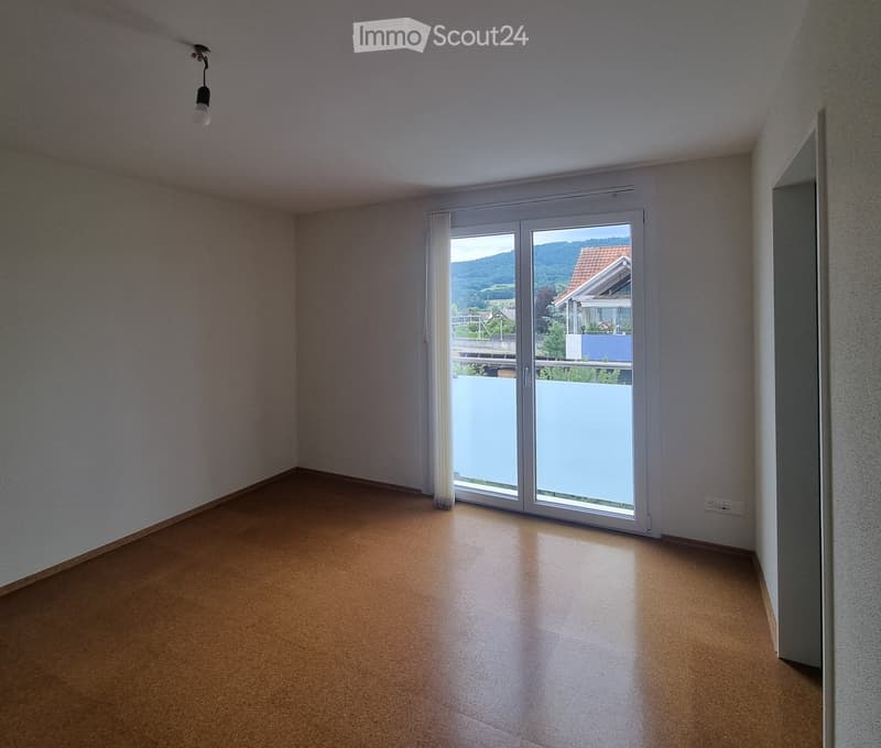 Empty room with light-colored walls, wooden flooring, and a large sliding glass door leading to a balcony with a scenic mountain view.