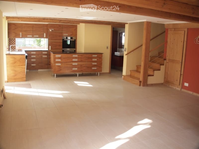 Open-plan kitchen and living area with wooden cabinets, a sink, an oven, and a staircase leading to another level.