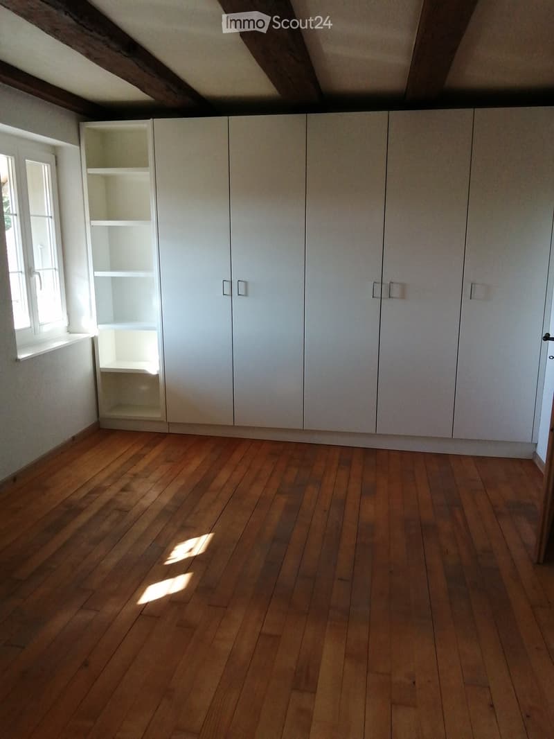 Empty room with wooden flooring, white built-in wardrobes, and a window letting in natural light.
