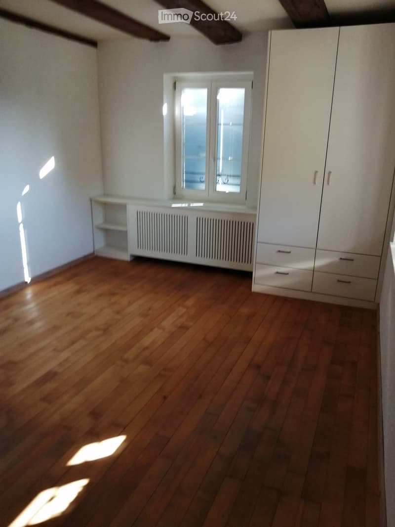 Empty room with wooden flooring, white walls, built-in white cabinetry, and a window with double glass panes.