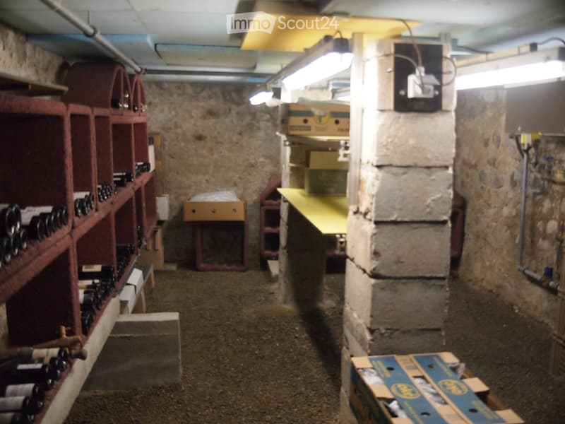 Wine cellar with stone walls, wooden racks filled with wine bottles, and storage boxes on the floor.