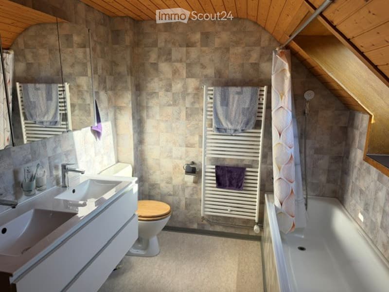 Modern bathroom with two sinks, a toilet, a bathtub, a radiator with towels, and a mirror above the sinks.