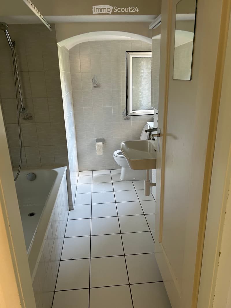 Modern bathroom with white tiled floor and walls, featuring a bathtub, toilet, sink, and mirror.
