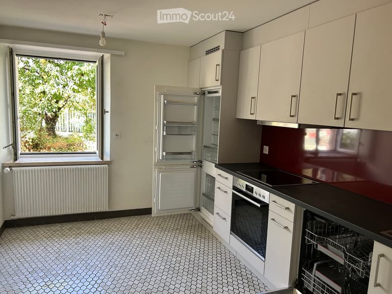Modern kitchen with white cabinets, stainless steel appliances, and a dark countertop. Features an open refrigerator, oven, and dishwasher, with a window offering a view of greenery.