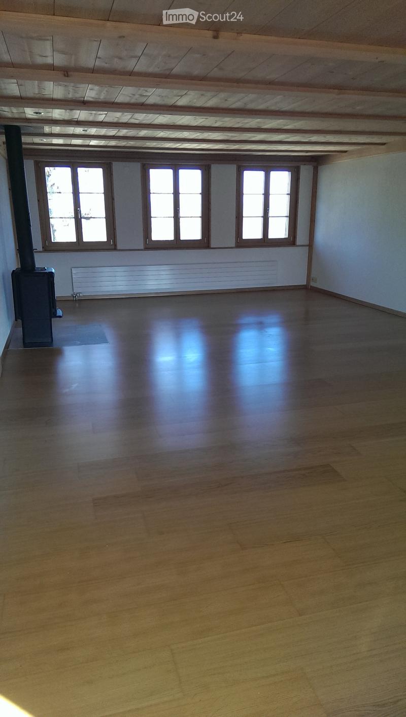 Empty room with wooden flooring, large windows, and a central heating system. No furniture or equipment present.