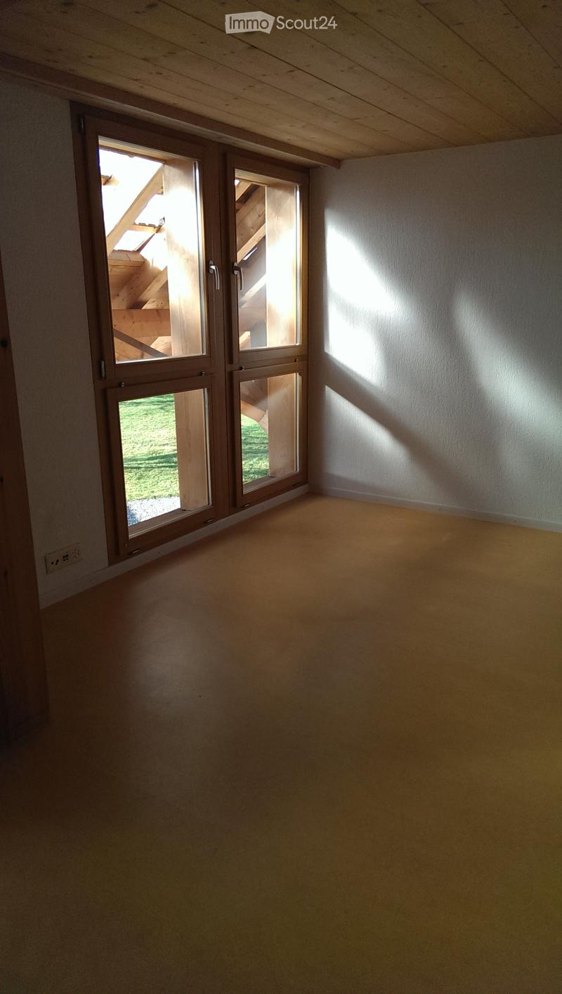 Empty room with wooden floor, white walls, and large windows with wooden frames, allowing natural light to enter.