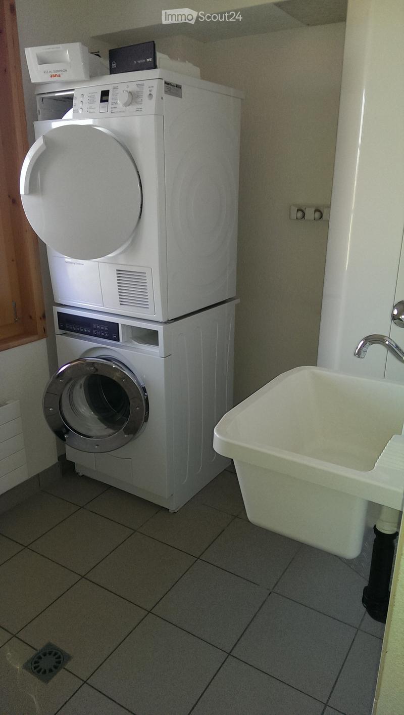 Bathroom with a washing machine and a sink, tiled floor, and a wooden door visible on the left side.