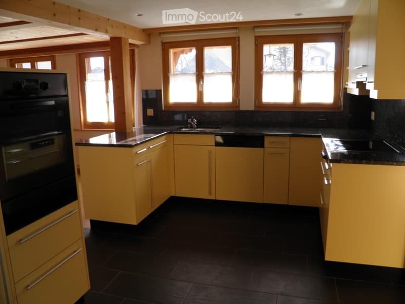 Bright kitchen with yellow cabinets, black countertops, and large windows. Features a sink, faucet, and built-in oven.