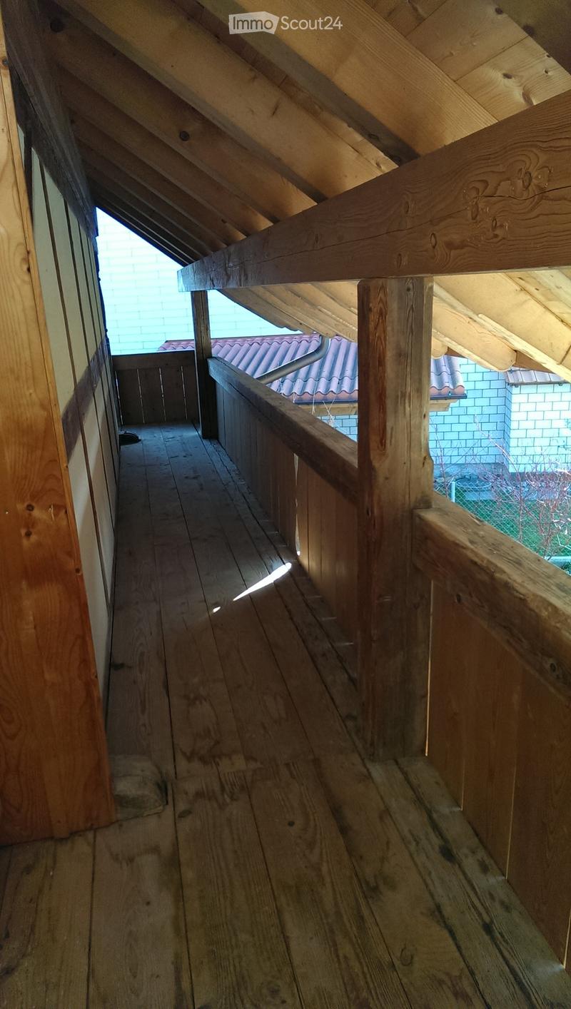 Wooden staircase with handrail and exposed wooden beams, leading to an attic space with visible roof structure and skylight.