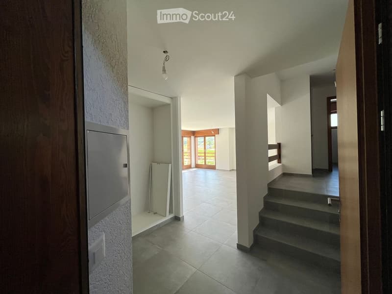 Empty hallway with tiled flooring, white walls, and a staircase leading upwards. A glass door at the end opens to an outdoor area.