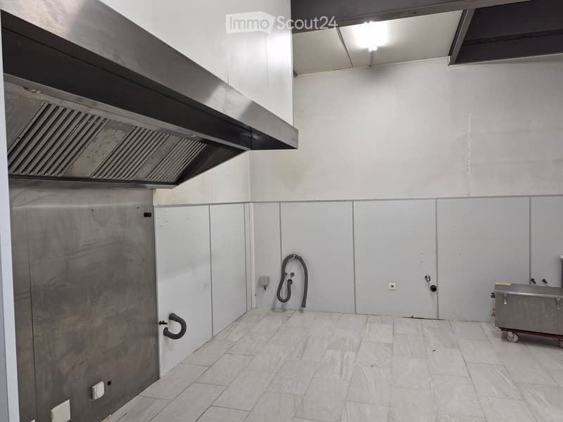 Empty room with white tiled floor, stainless steel walls, and a large exhaust hood. No furniture or equipment present.