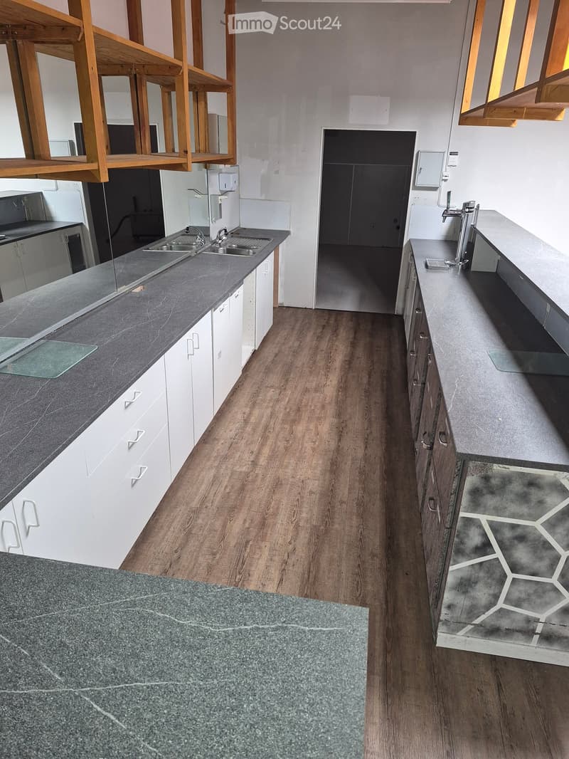Modern kitchen with white cabinets, dark countertops, and a wooden floor. Features a sink with a faucet and built-in cabinets.
