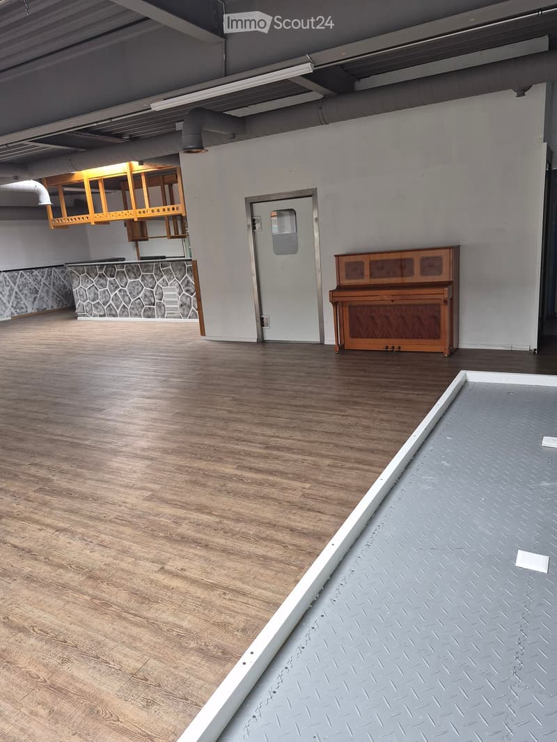 Empty room with wooden flooring, a piano, and a wooden shelf mounted on the wall.