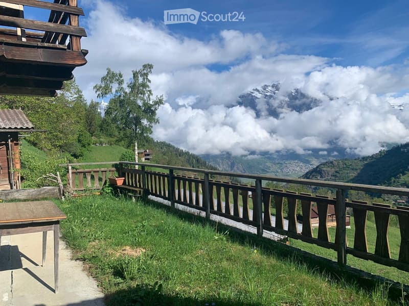 A wooden balcony overlooking a scenic mountain landscape with a wooden fence, a small table, and a potted plant.