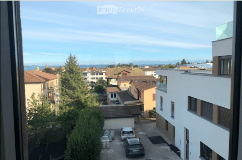 Balcony view overlooking a residential area with houses, trees, and parked cars.
