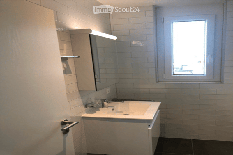 Modern bathroom with a white tiled wall, a sink with a mirror above it, and a window letting in natural light.