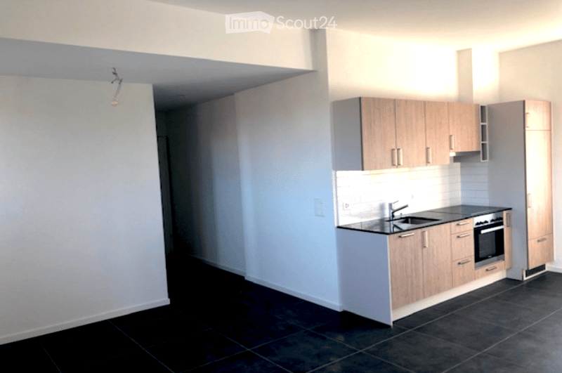 Modern kitchen with light wood cabinets, black tiled floor, stainless steel sink, and built-in oven.