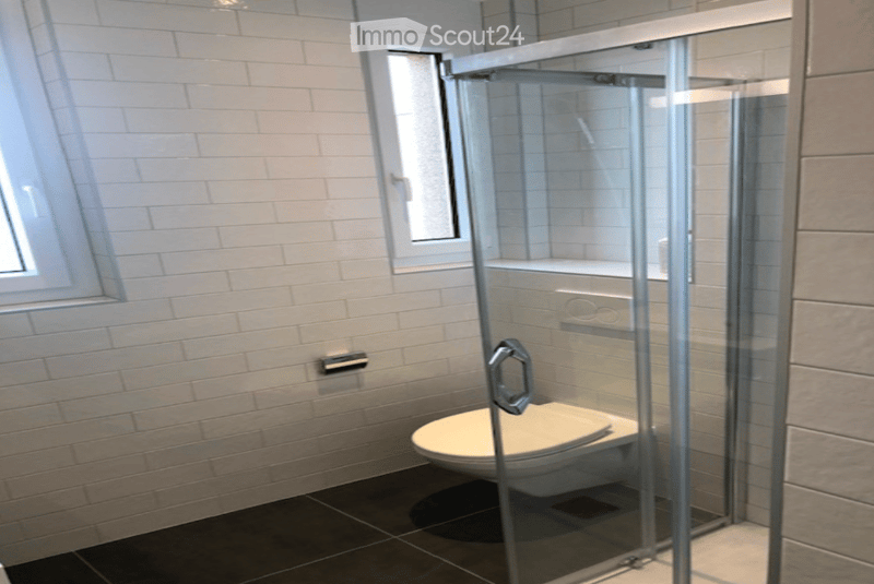 Modern bathroom with white tiled walls, dark tiled floor, a toilet, and a glass-enclosed shower area.