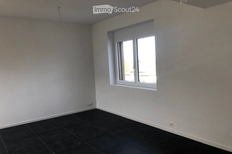 Empty room with dark tiled floor, white walls, and a single window with white frame. No furniture or equipment visible.