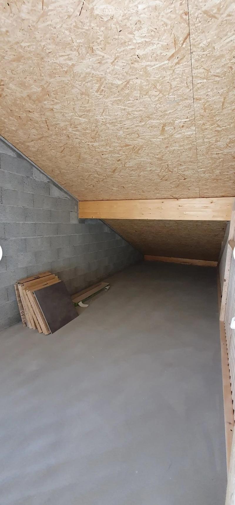 Empty attic space with exposed wooden beams and grey concrete floor. No furniture or equipment present.