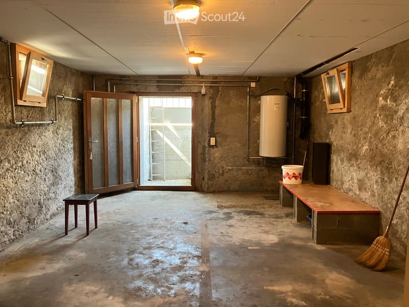 Empty room with concrete walls and floor, wooden door, small window, bench, and broom.