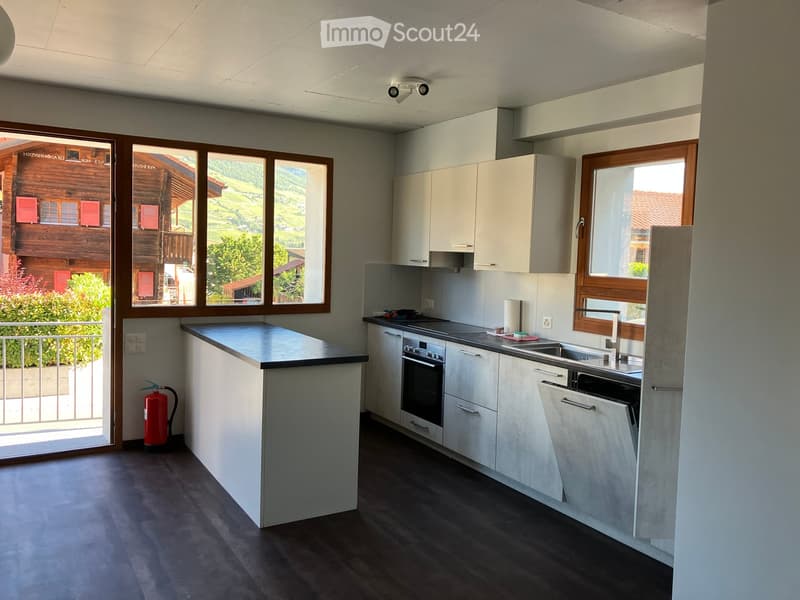 Modern kitchen with white cabinets, dark countertops, and stainless steel appliances, including an oven and sink. Large windows offer a scenic view of the countryside.