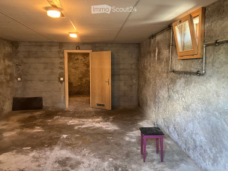 Empty room with concrete walls and floor, wooden door, small window, and a single purple stool.