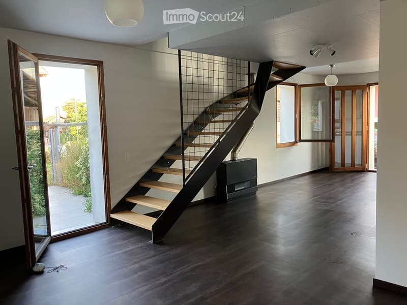 Modern hallway with dark wooden flooring, a staircase with wooden steps and metal railing, and large glass doors leading to an outdoor area.