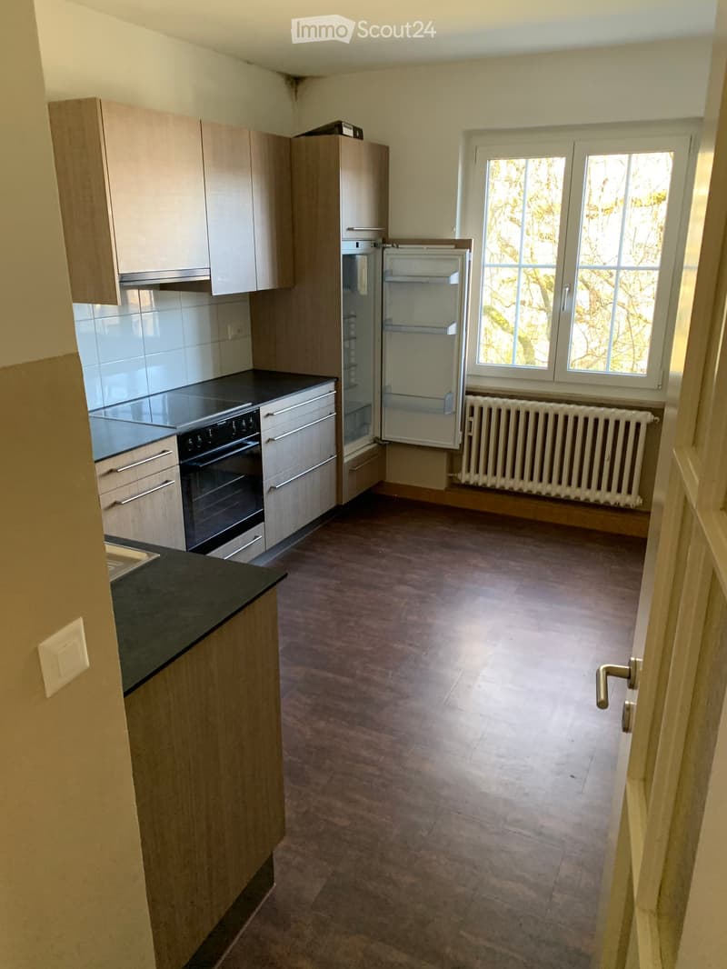 wooden kitchen cabinets, black countertop, white fridge, oven, sink, window with grill, wooden flooring
